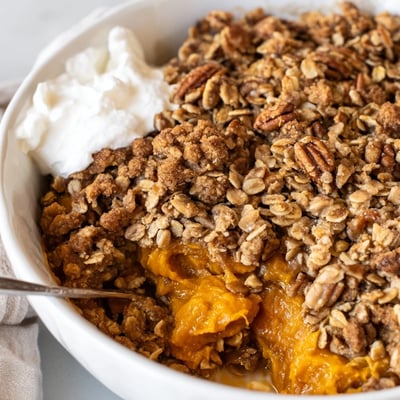 Warm pumpkin pie crisp scooped into bowls topped with whipped cream