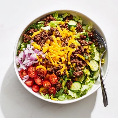 Deconstructed burger bowls feature juicy ground beef topped with melted cheese and fresh greens.